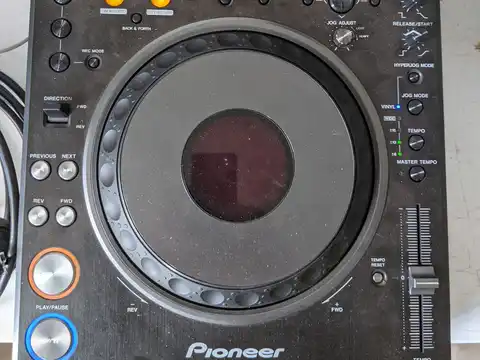 The Pioneer DVJ-1000 professional DVD/CDJ player powered up and playing, seen from above with its jog wheel, transport controls, tempo fader and lit display.